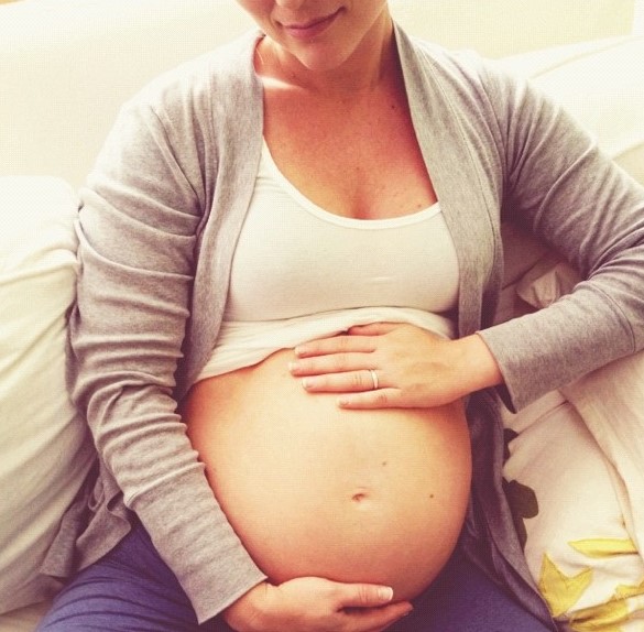 a pregnant woman holding her hands on her belly looking happy and content