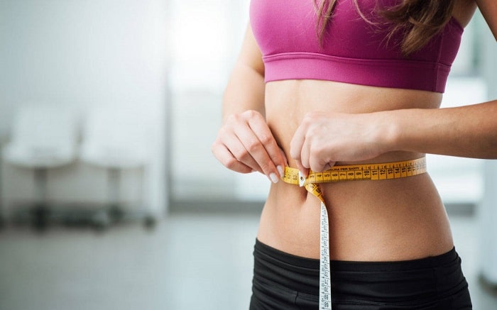 a slim woman measuring her abdomen size