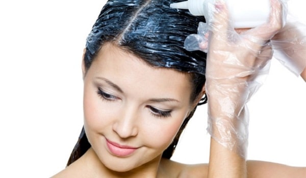 Brunette woman smiling while applying hair dye