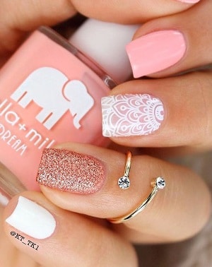 A pink nail polish bottle in someone's hand having pink nail polish on fingernails, white sticker, glitter and white nail polish
