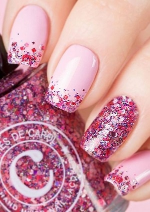 Light shade of pink on nails with darker shad of pink glitter at the tip and pink glitter on the ring finger