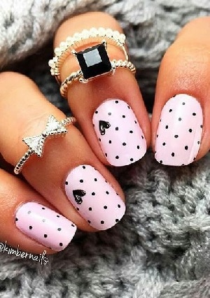 Pink nail polish with black little spots and black hearts, holding a gray woolen sweater