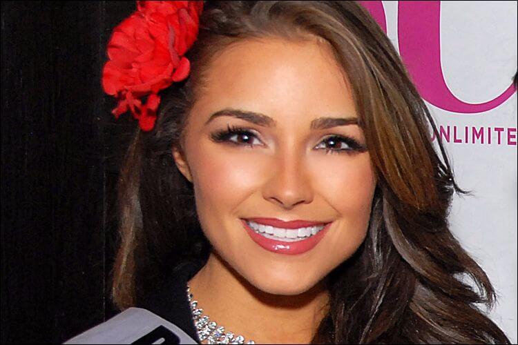 Close shot of Olivia Culpo smiling, with a red flower in her hair